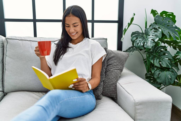 Giovane donna latina che legge libro bere caffè a casa - Foto, immagini