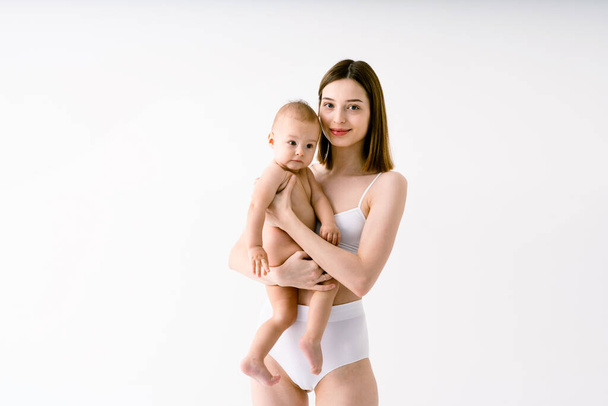 Szczęśliwa kobieta trzymająca swoje dziecko na kolorowym tle - młoda kobieta w bieliźnie dbająca o swojego synka - Ciąża, macierzyństwo, ludzie i koncepcja oczekiwania - Zdjęcie, obraz