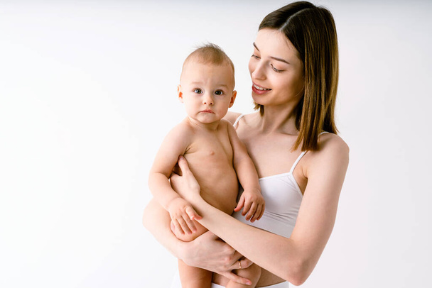 Happy woman holding her baby  on colored background -  Young woman wearing underwear taking care of her little son  - Pregnancy, motherhood, people and expectation concept - Foto, imagen