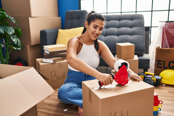 Молода іспаномовна жінка посміхається впевнено упаковує кухонну коробку в новому будинку
 - Фото, зображення