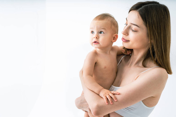 Happy woman holding her baby  on colored background -  Young woman wearing underwear taking care of her little son  - Pregnancy, motherhood, people and expectation concept - Zdjęcie, obraz