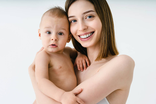 Happy woman holding her baby  on colored background -  Young woman wearing underwear taking care of her little son  - Pregnancy, motherhood, people and expectation concept - Фото, изображение