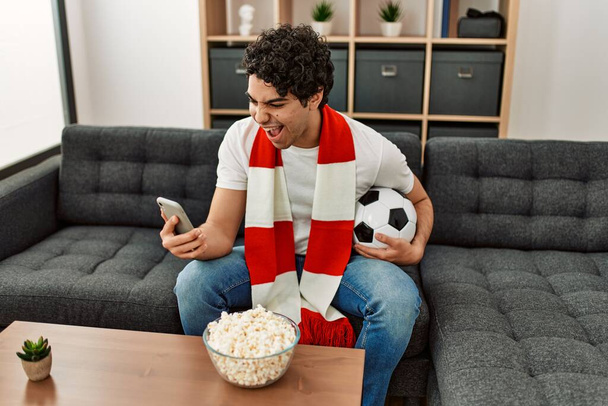 Giovane uomo ispanico guardando partita di calcio e squadra di supporto a casa. - Foto, immagini