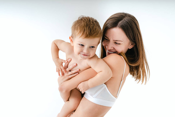 幸せな女性保持彼女の赤ちゃんに色の背景-若い女性を身に着けている下着彼女の小さな息子の世話-妊娠,母親,人々と期待の概念 - 写真・画像