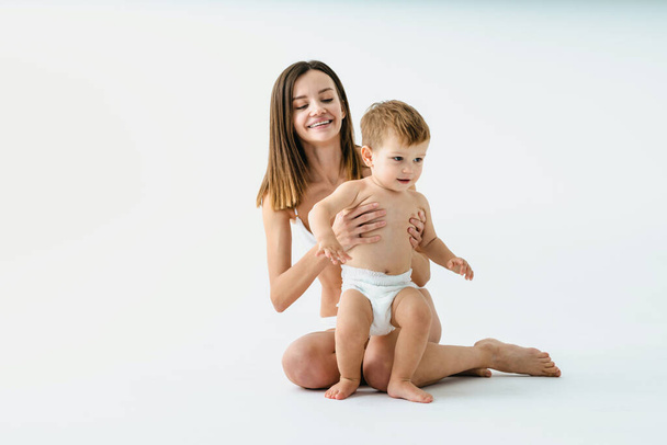 Happy woman holding her baby  on colored background -  Young woman wearing underwear taking care of her little son  - Pregnancy, motherhood, people and expectation concept - Foto, Imagem