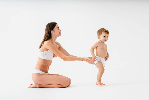 Happy woman holding her baby  on colored background -  Young woman wearing underwear taking care of her little son  - Pregnancy, motherhood, people and expectation concept - Foto, Imagen