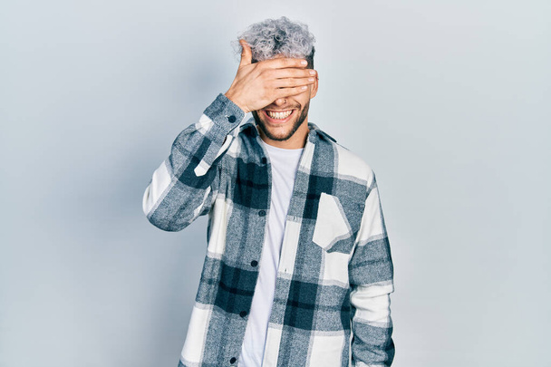 Young hispanic man with modern dyed hair wearing casual shirt smiling and laughing with hand on face covering eyes for surprise. blind concept.  - Fotoğraf, Görsel