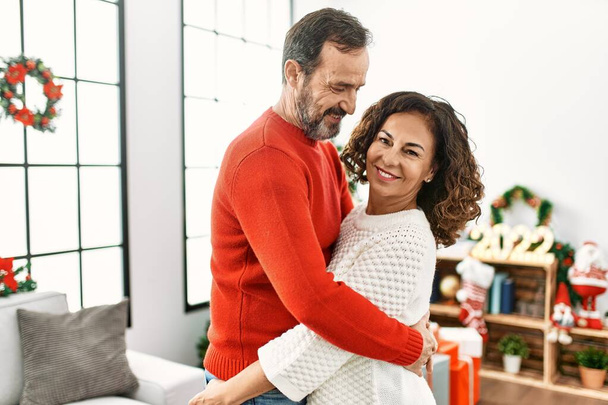 Middle age hispanic couple smiling happy and hugging celebrating christmas at home. - Foto, Imagem