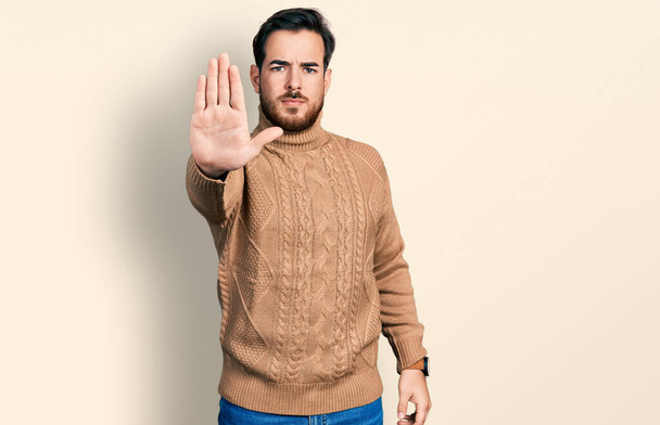 A fiatal spanyol férfi alkalmi ruhában abbahagyja az éneklést tenyérrel. figyelmeztető kifejezés negatív és komoly gesztussal az arcon.  - Fotó, kép