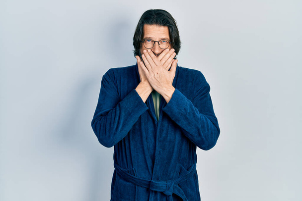 Middle age caucasian man wearing bathrobe and glasses shocked covering mouth with hands for mistake. secret concept.  - Fotó, kép