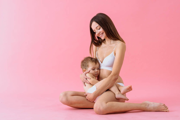 Happy woman holding her baby  on colored background -  Young woman wearing underwear taking care of her little son  - Pregnancy, motherhood, people and expectation concept - 写真・画像
