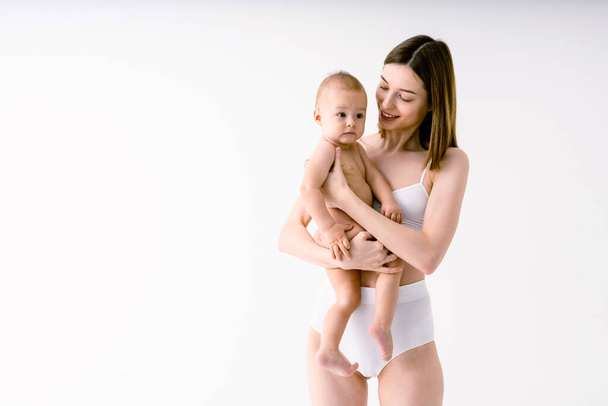 Happy woman holding her baby  on colored background -  Young woman wearing underwear taking care of her little son  - Pregnancy, motherhood, people and expectation concept - Photo, Image