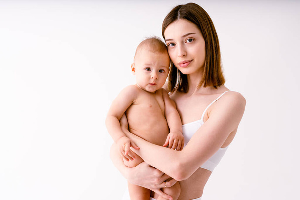 Happy woman holding her baby  on colored background -  Young woman wearing underwear taking care of her little son  - Pregnancy, motherhood, people and expectation concept - Φωτογραφία, εικόνα