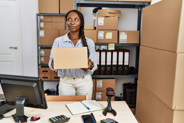 African woman working at small business ecommerce holding box smiling looking to the side and staring away thinking.  - Φωτογραφία, εικόνα