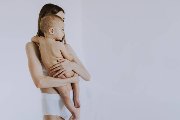 Happy woman holding her baby  on colored background -  Young woman wearing underwear taking care of her little son  - Pregnancy, motherhood, people and expectation concept - Photo, Image