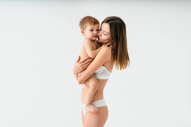 Happy woman holding her baby  on colored background -  Young woman wearing underwear taking care of her little son  - Pregnancy, motherhood, people and expectation concept - Foto, immagini