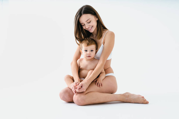 Happy woman holding her baby  on colored background -  Young woman wearing underwear taking care of her little son  - Pregnancy, motherhood, people and expectation concept - Fotografie, Obrázek