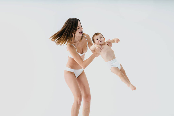 Happy woman holding her baby  on colored background -  Young woman wearing underwear taking care of her little son  - Pregnancy, motherhood, people and expectation concept - Foto, afbeelding
