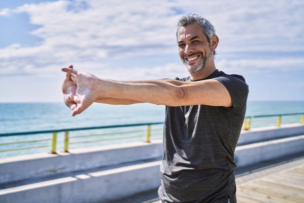 Middelbare leeftijd Spaanse man draagt sportkleding die zich uitstrekt aan de kust - Foto, afbeelding