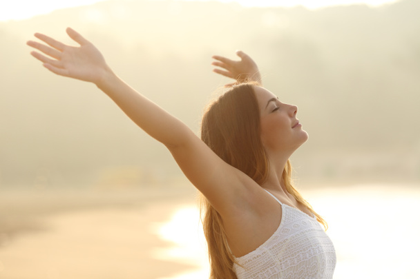 Relaxed woman breathing fresh air raising arms at sunrise - Foto, afbeelding