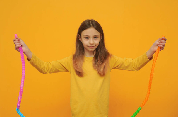 klein meisje in gele kleren speelt met trendy speelgoed pop tube - Foto, afbeelding