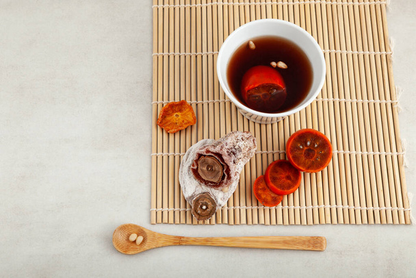 Sujeonggwa - Traditional Korean Persimmon tea or fruits punch in white bowl on stone table. Top view, selective focus. - Fotoğraf, Görsel