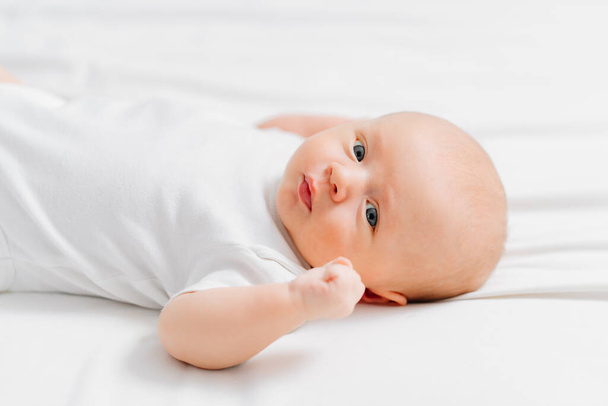 cute baby wearing a white t-shirt on a white sheet. pediatrics - Fotó, kép