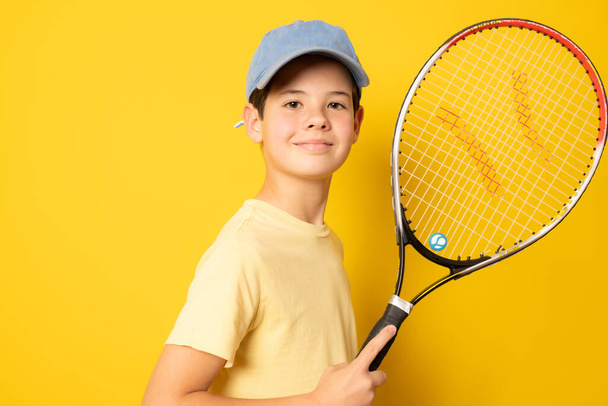 Smiling boy playing tennis holding racket isolated on yellow background - Photo, Image