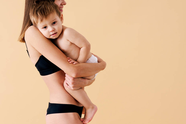 Happy woman holding her baby  on colored background -  Young woman wearing underwear taking care of her little son  - Pregnancy, motherhood, people and expectation concept - Fotoğraf, Görsel