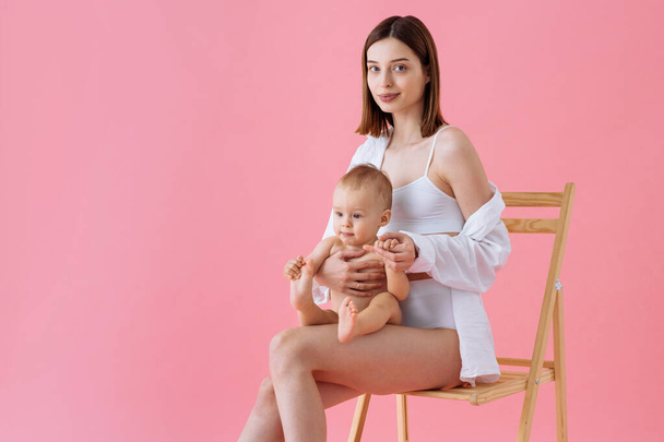 Happy woman holding her baby  on colored background -  Young woman wearing underwear taking care of her little son  - Pregnancy, motherhood, people and expectation concept - Fotoğraf, Görsel