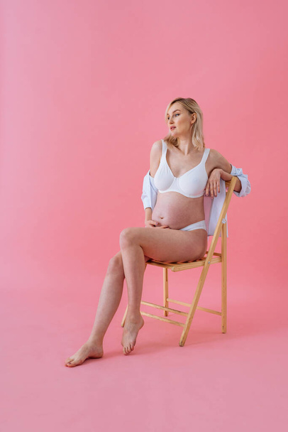 Happy pregnant woman with big belly on colored background -  Young woman wearing underwear expecting a baby - Pregnancy, motherhood, people and expectation concept - - Foto, immagini