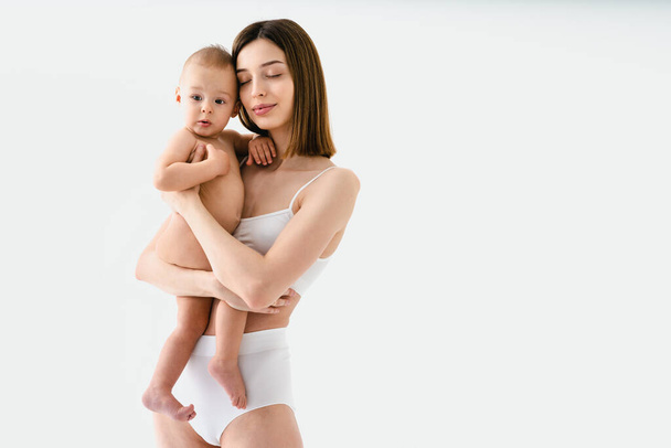Happy woman holding her baby  on colored background -  Young woman wearing underwear taking care of her little son  - Pregnancy, motherhood, people and expectation concept - Foto, afbeelding