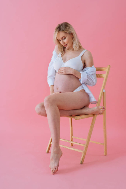 Happy pregnant woman with big belly on colored background -  Young woman wearing underwear expecting a baby - Pregnancy, motherhood, people and expectation concept - - Zdjęcie, obraz