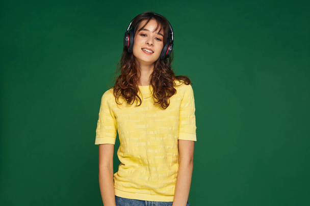 Happy calm young girl wearing headphones listening to music enjoy good sound chilling on green studio background - Foto, immagini
