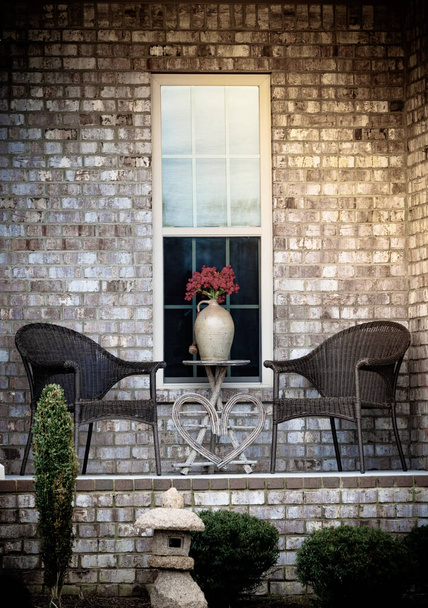 Romantically arranged lawn chairs, table and red flowers vase in front of house window. - 写真・画像