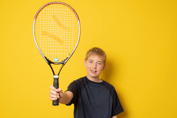 Smiling boy playing tennis holding racket isolated on yellow background - Фото, изображение