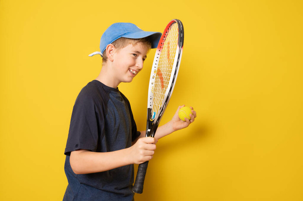 Smiling boy playing tennis holding racket isolated on yellow background - Foto, immagini