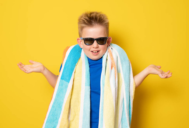 Cute doubtful boy wearing sunglasses in summer outfit standing over yellow background. - Fotó, kép