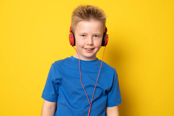Netter Junge, der Kopfhörer trägt und isoliert auf gelbem Hintergrund Musik hört. - Foto, Bild