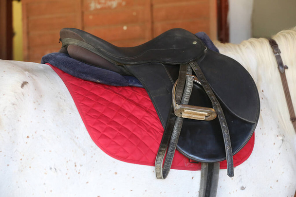 Close up of a sport horse saddle. Old quality leather saddle ready for show jumping  event. Equestrian sport background outdoors - Fotó, kép