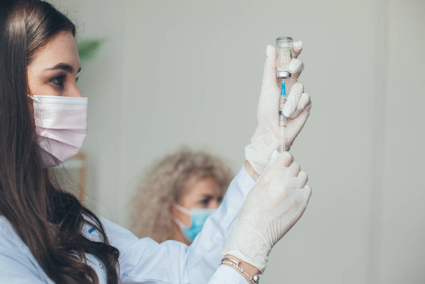 Κοντινό πλάνο πορτραίτο μιας νοσοκόμας που κρατάει και γεμίζει το εμβόλιο με σύριγγα. ανοσοποίηση του ιού του κερατοειδούς. - Φωτογραφία, εικόνα