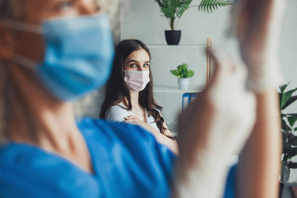 Sestra v masce obličeje a držící stříkačku s vakcínou covid-19 v nemocnici. Očkování virem korony. - Fotografie, Obrázek