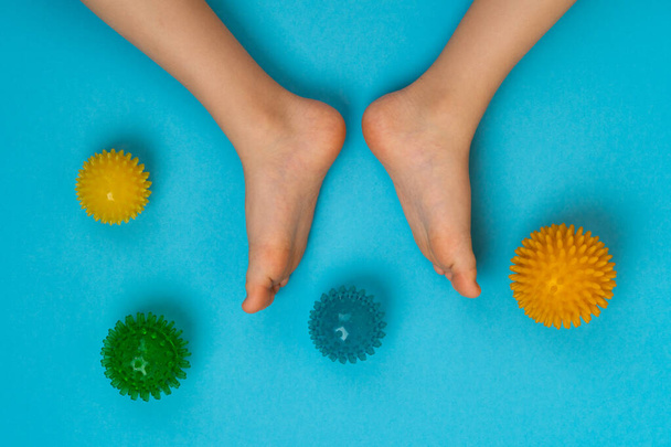 цветные игольные шарики для массажа и физиотерапии на синем фоне с изображением детских ног, концепция профилактики и лечения галлюкса вальгуса - Фото, изображение