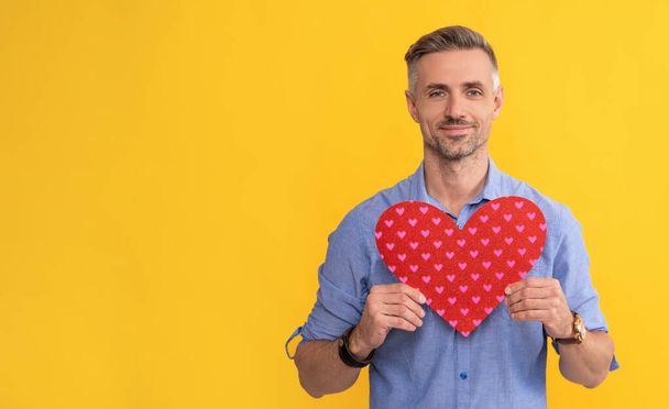 el hombre guapo sostiene el corazón del amor para el día de San Valentín en el fondo amarillo, espacio de copia, donación - Foto, imagen