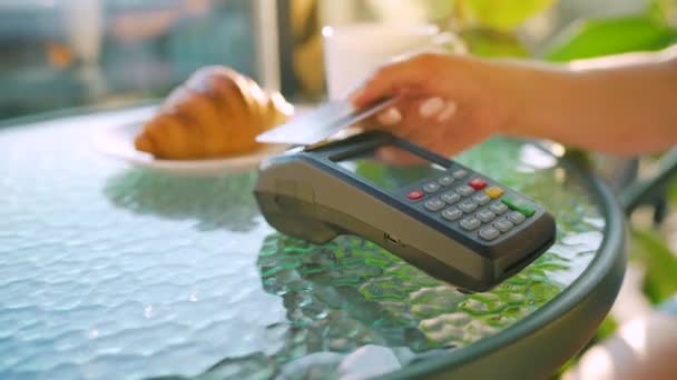 NFC luottokorttimaksu. Nainen maksaa kontaktittomalla luottokortilla NFC-tekniikalla maksaakseen tilauksen pankkipäätteellä kahvilassa. Langaton rahansiirto. Langaton maksu - Materiaali, video