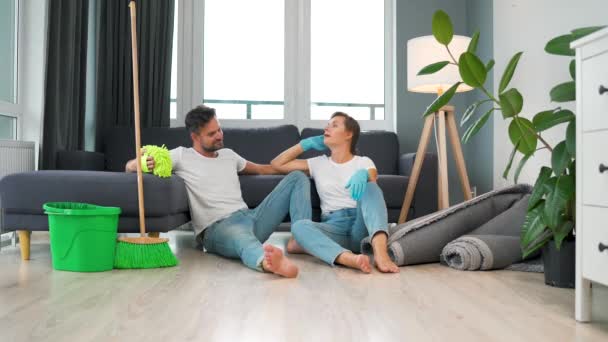 Tired couple sits on the floor in a room and high five each other after they finish cleaning the house. - Filmmaterial, Video
