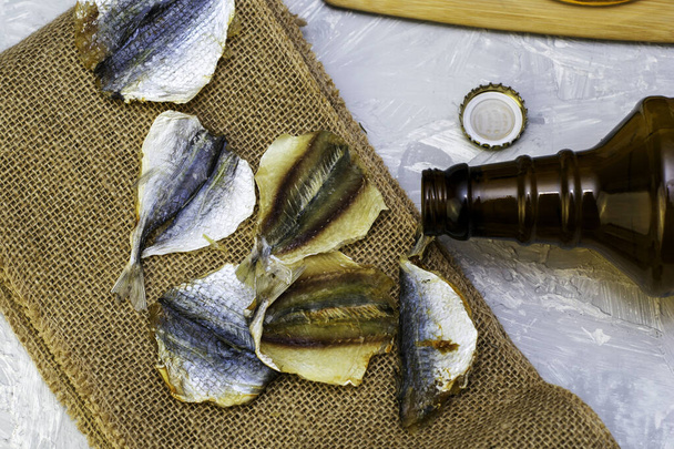 botella de cerveza vacía, corcho y pescado seco en arpillera - Foto, Imagen