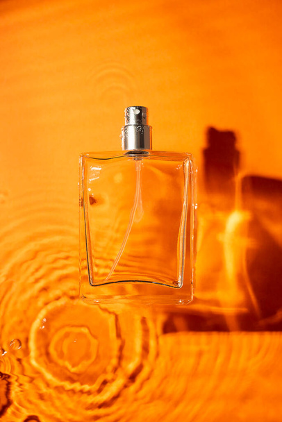 Transparent bottle of perfume on a orange water background. Fragrance presentation with daylight. Trending concept in natural materials with beauty shadow. Women's and men's essence. - Foto, Bild