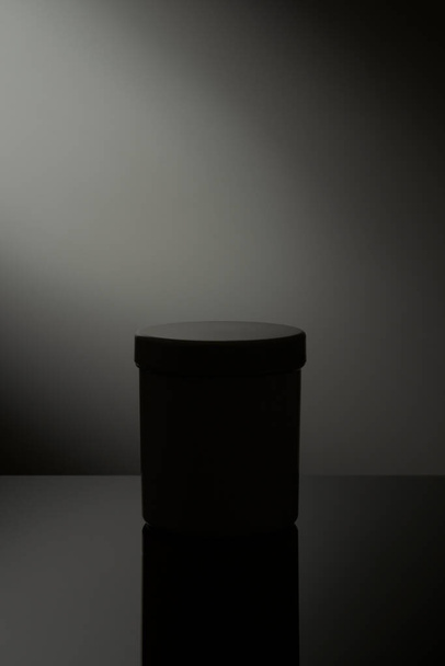 Низька світло-біла косметична банка з відображенням на сірому фоні
 - Фото, зображення