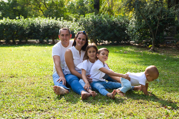 Портрет счастливых родителей с тремя детьми, лежащими в парке. Старшая дочь трансгендерная девочка. Концепция семьи счастливая объединенная семья с детьми. - Фото, изображение